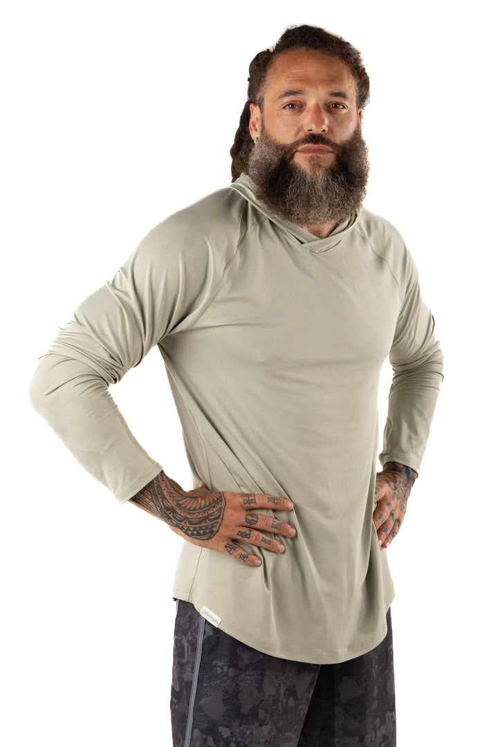 Male model with dreadlocks and tattoos wearing the Waihana Mariner Green Hooded Long Sleeve sun shirt in sage green, hands on hips against a white studio background.