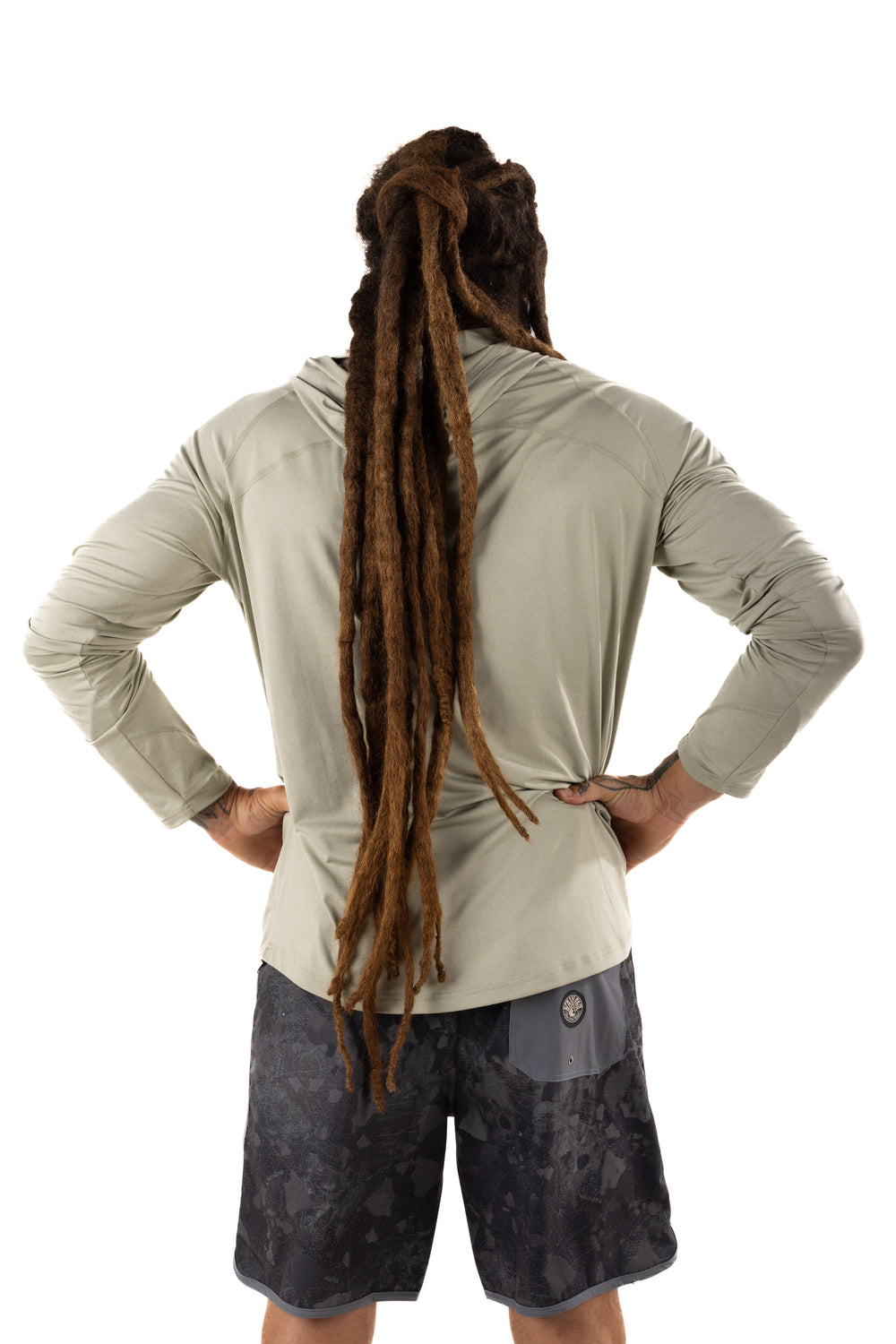 Back view of a man with long dreadlocks wearing the Waihana Mariner Green Hooded Long Sleeve sun shirt paired with dark camo board shorts on a white background.