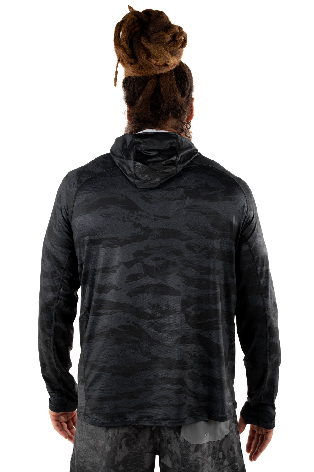 Back view of a male model with dreadlocks wearing the Waihana Tropicam Black long-sleeve hooded sun shirt in a dark camouflage pattern, styled with matching camo shorts on a white background.